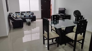 Un salon moderne avec une table à manger en verre, des chaises noires, un canapé et un téléviseur.