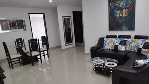 Un salon moderne avec un canapé noir, une table basse en verre et un coin repas comprenant une table et des chaises en verre.