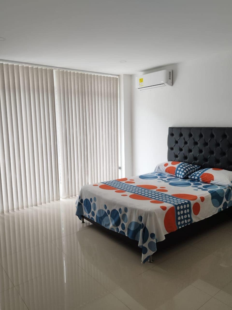 Ein Schlafzimmer mit einem Bett, einem Fenster mit Jalousien und einer Klimaanlage.