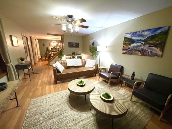 Un salon avec un canapé, deux tables basses, un fauteuil et un tableau accroché au mur.