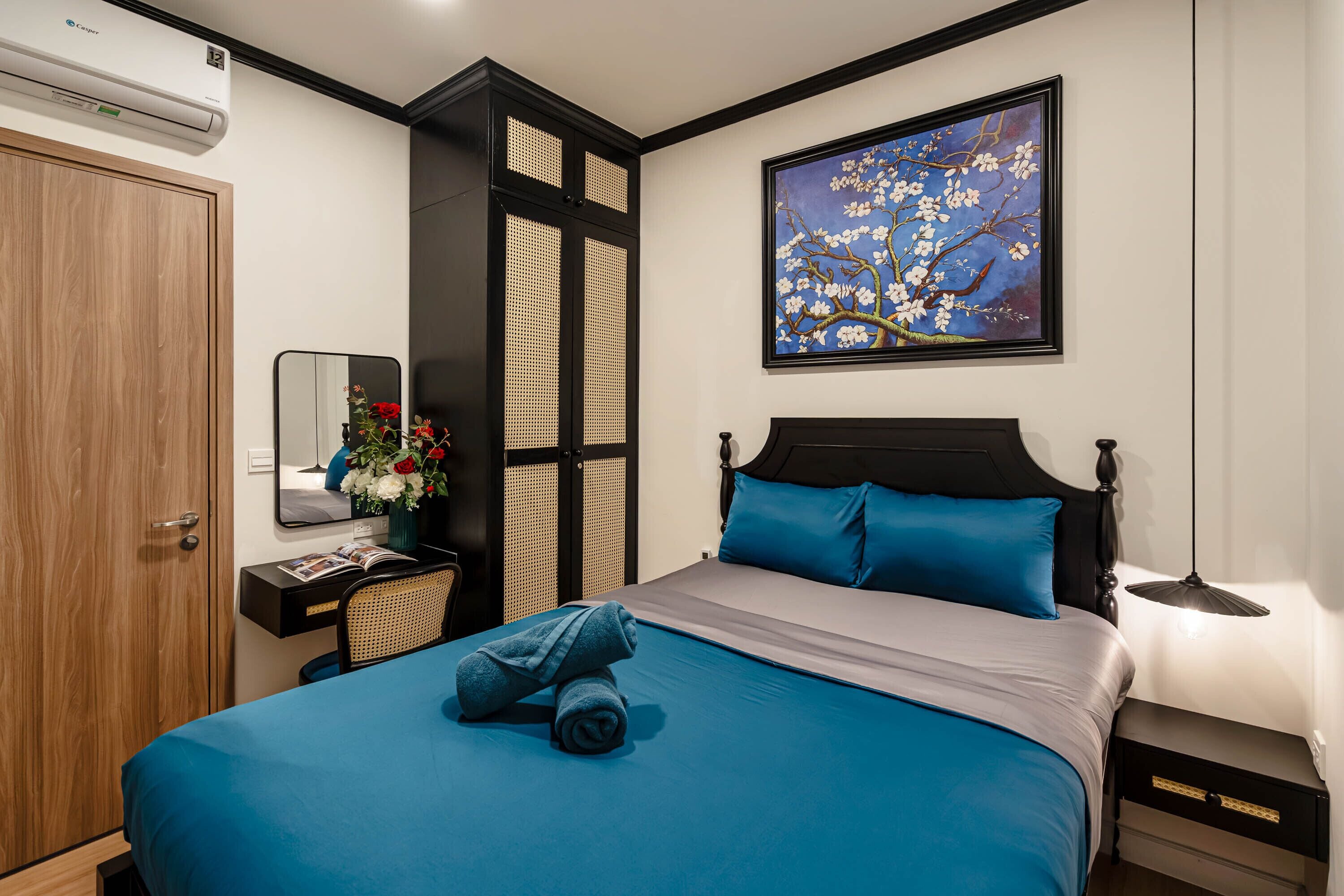 A neatly arranged bedroom with a bed, a bedside table, a nightstand, a mirror, and a wall-mounted air conditioner.