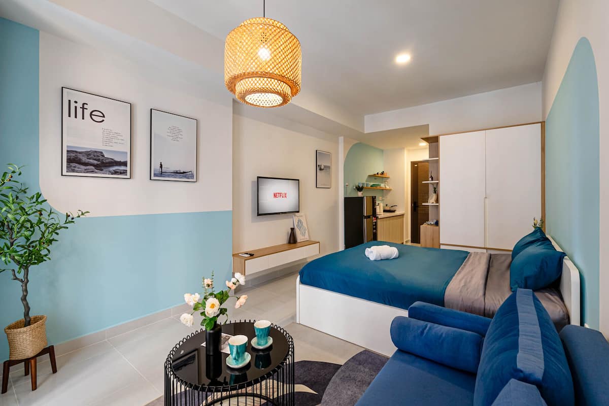 Ein modernes Hotelzimmer mit Bett, Sofa und einem kleinen Tisch mit Blumen. An den Wänden hängen gerahmte Bilder und es gibt einen Fernseher.