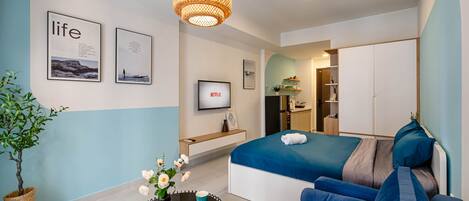 Una habitación de hotel moderna con una cama, un sofá y una mesita con un jarrón de flores. Hay cuadros en la pared y un televisor.