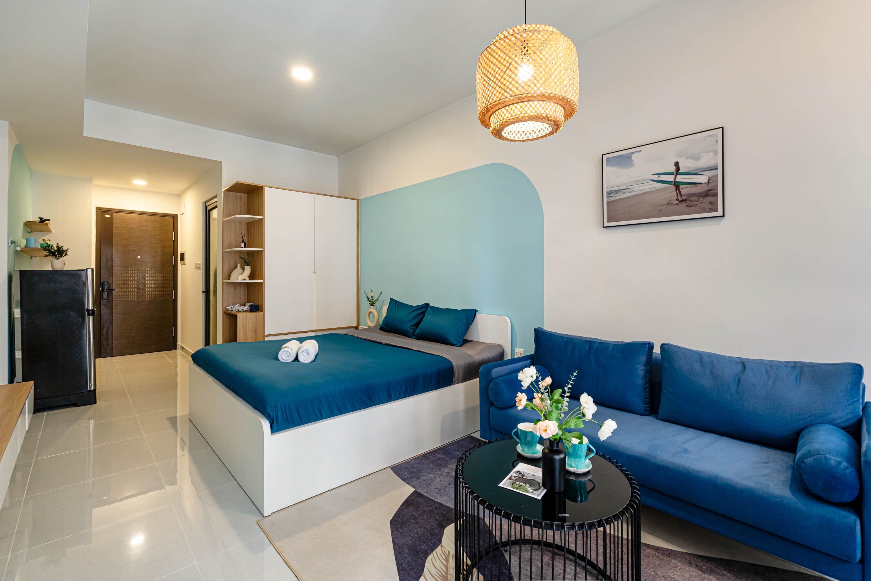 A modern bedroom with a bed, a sofa, a small table, and a hanging light fixture.