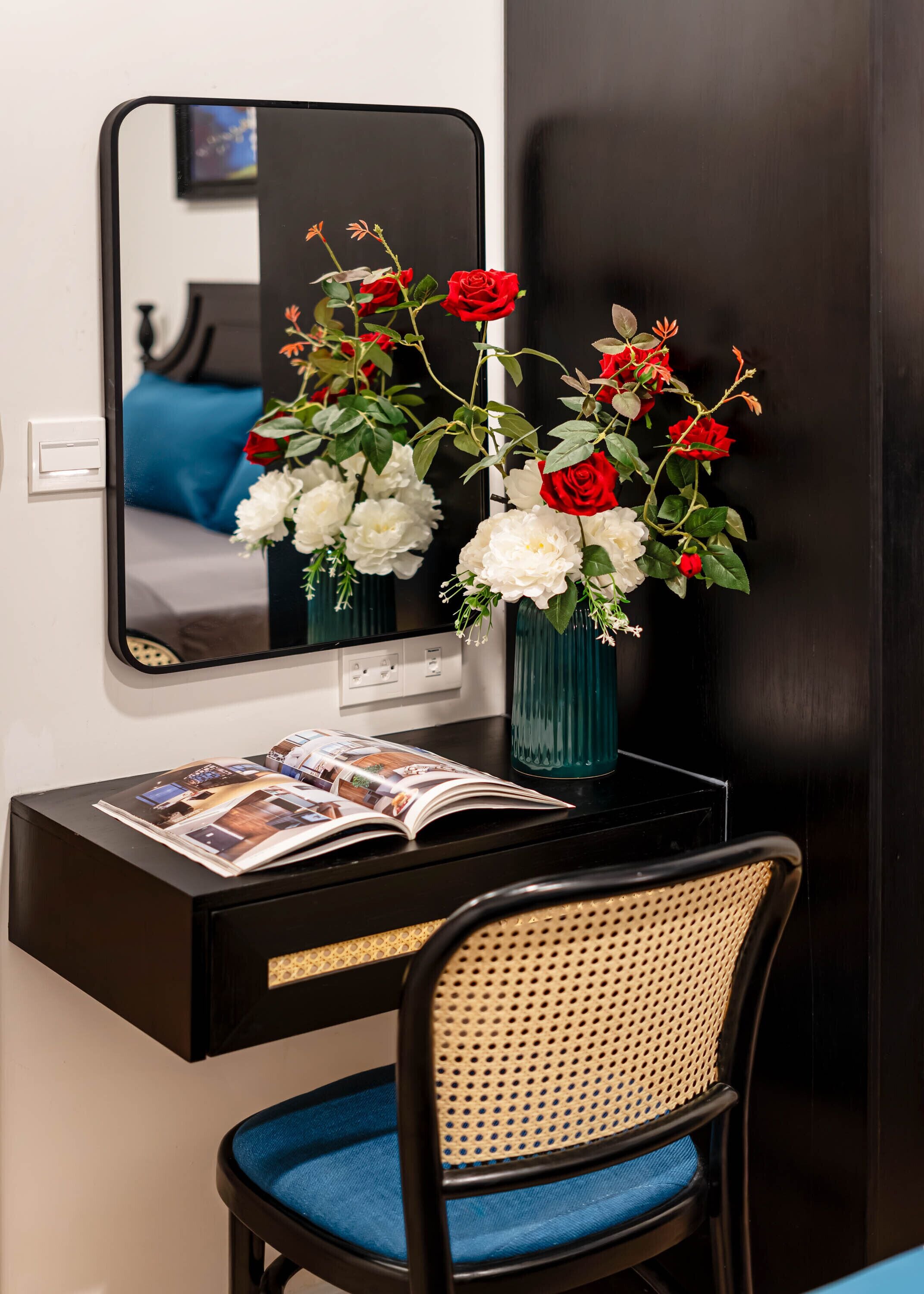 A desk with a mirror, a vase with flowers, and a magazine.