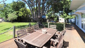 An outdoor wooden deck with a table and chairs, surrounded by trees and a basketball hoop.