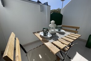 Une petite terrasse extérieure avec une table en bois, deux chaises et un banc.