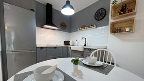 A modern kitchen with white cabinets, a stainless steel refrigerator, a microwave, and a dining table set with white dishes. - Buganvilla house, super wifi, sunny terrace (Playa Blanca)