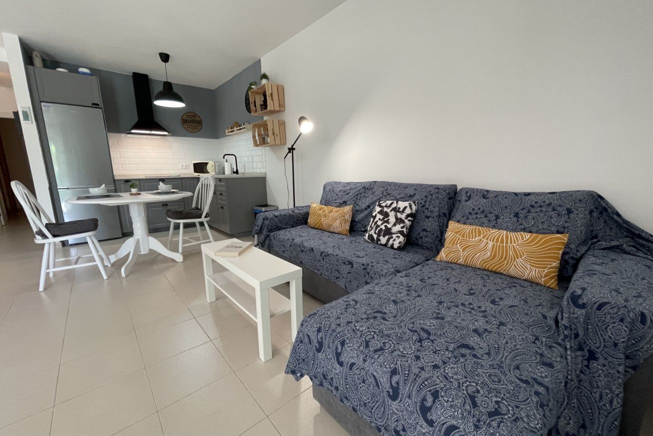 Ett kompakt bostadsutrymme med ett litet kök, en matplats och en soffa med mönstrat tyg.