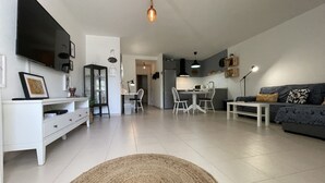 A modern living room with a TV, white furniture, a dining area with chairs, and a kitchen in the background. - Buganvilla house, super wifi, sunny terrace (Playa Blanca)