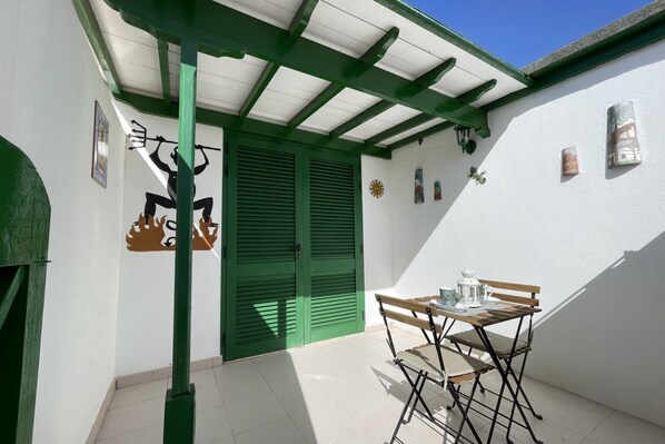 Une terrasse avec une table et des chaises, des volets verts et un mur décoré d’œuvres d’art.