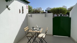 A small outdoor patio with a table and chairs, a green gate, and a white wall with a sign. - Buganvilla house, super wifi, sunny terrace (Playa Blanca)