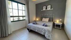 A bedroom with a bed, two bedside tables, a window with curtains, and a wall-mounted shelf with framed pictures. - Buganvilla house, super wifi, sunny terrace (Playa Blanca)
