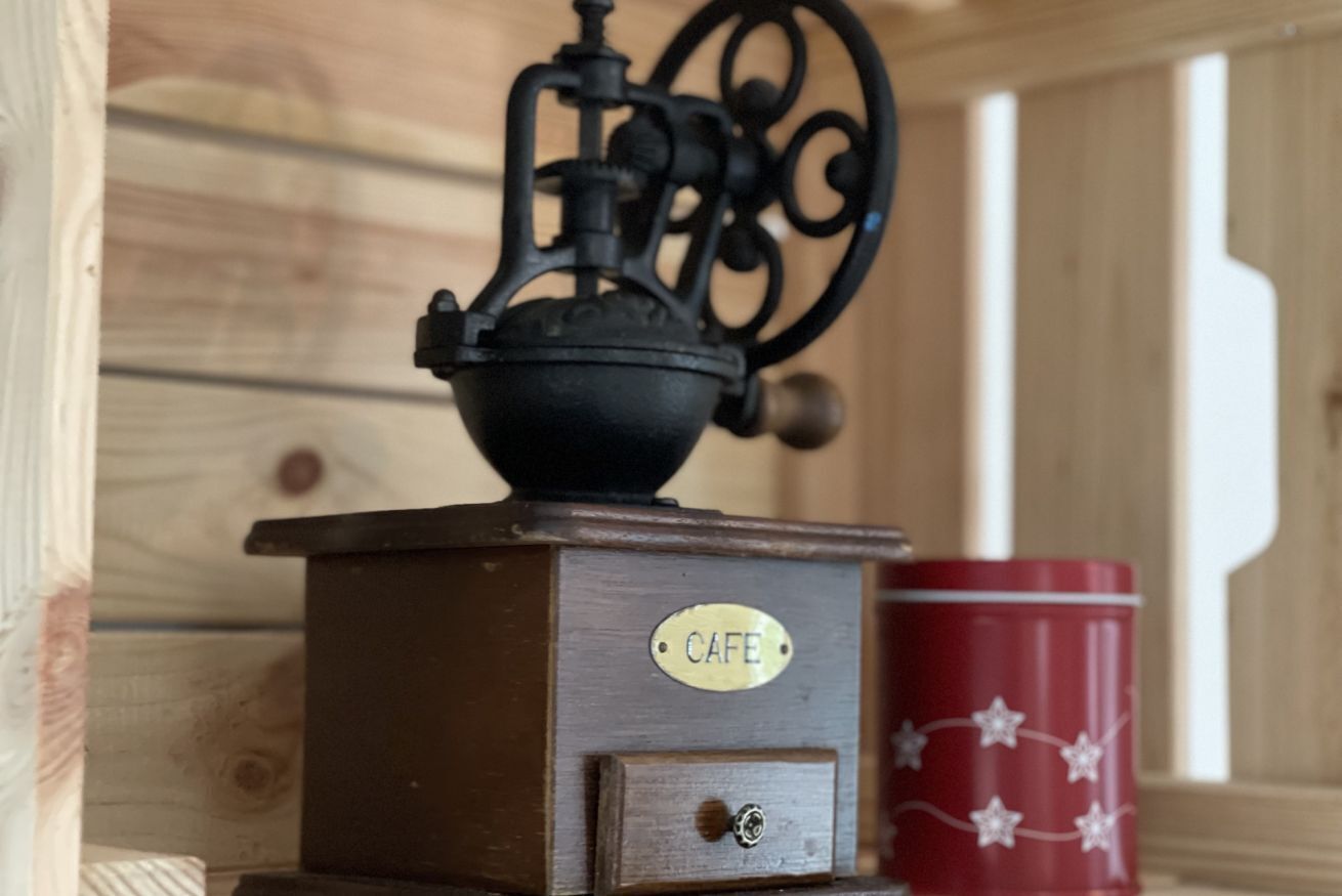 Un molinillo de café antiguo con la etiqueta 'CAFE', una lata roja con estrellas y un fondo de madera.