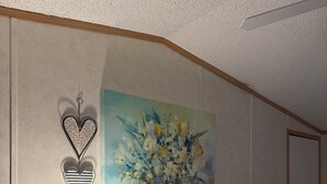 Una camera da letto con un letto, un comodino con una lampada, una decorazione a forma di cuore appesa al muro e un quadro con dei fiori.