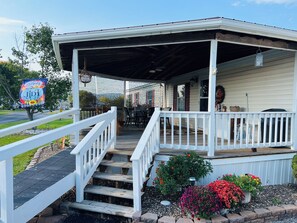 A covered porch with a white railing, wooden steps, and potted plants. - Cozy Mobile Home In Just the Right Place. (Moorefield)