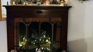 Un camino con mensola decorata da casette e figurini, un quadro incorniciato sopra e una ghirlanda appesa al muro.