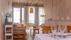 Ein gemütliches Zimmer mit Holzboden, einem mit Gläsern gedeckten Esstisch, einem Korbstuhl und einem Bücherregal.