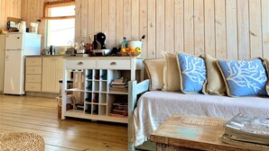 Ein gemütliches Zimmer mit Holzboden, einem weißen Sofa mit blauen Kissen, einem kleinen Holztisch und einer weißen Schrank mit Regalen.