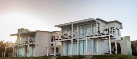 Una casa moderna de dos pisos con un balcón en el piso superior, un espacio exterior cubierto y una escalera que conduce a la entrada.
