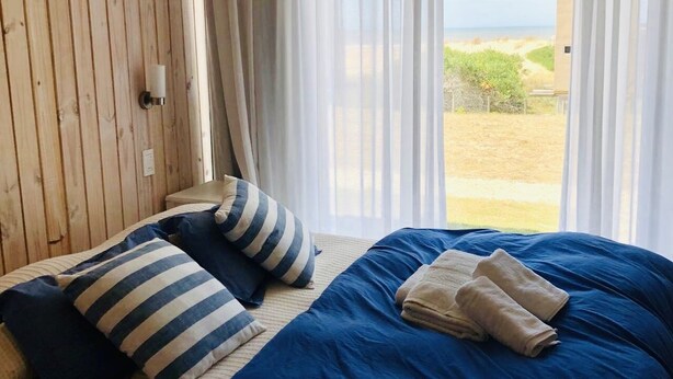 Ein Schlafzimmer mit einem großen Bett, gestreiften Kissen und Blick ins Freie.