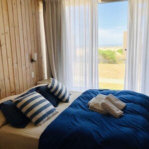 A bedroom with a large bed, striped pillows, and a view of the outdoors. - Las Marinas BH  (La Pedrera)
