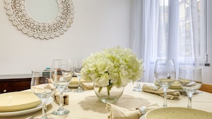 Una mesa de comedor dispuesta con platos, vasos y un jarrón con flores blancas.