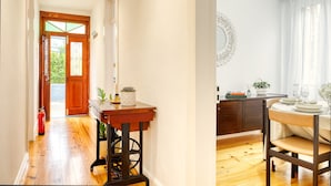 Un pasillo con piso de madera que conduce a una habitación con puerta de madera. Hay una mesa con un florero y una vela encima.