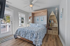 Un dormitorio con cama, ventilador de techo, estantería y ventana.