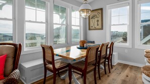 A dining area with a wooden table and wicker chairs, large windows, and a hanging light fixture.