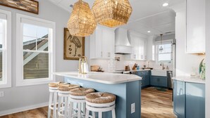 A modern kitchen with white and blue cabinets, a central island with stools, and a hanging light fixture.