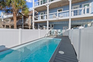 Un área de piscina con muelle de madera, una palmera y un edificio de varios pisos con balcones.