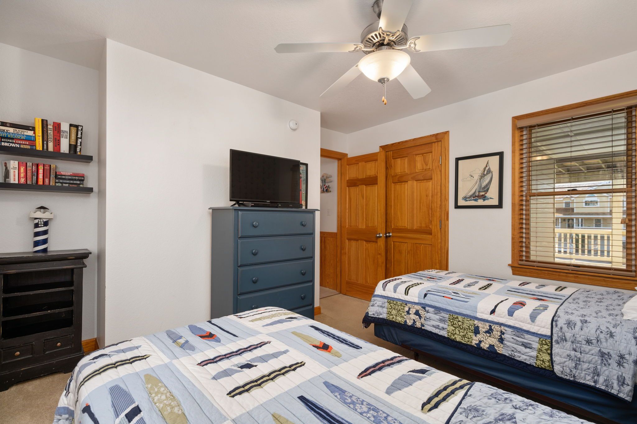 A bedroom with two beds, a TV on a dresser, wooden doors, and a window with blinds.