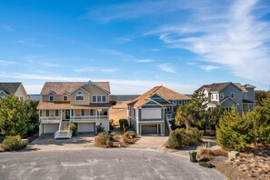 A residential neighborhood with houses featuring front porches, garages, and a clear sky. - Seas The Day: Private Hot Tub, Amazing Sunsets (Nags Head)