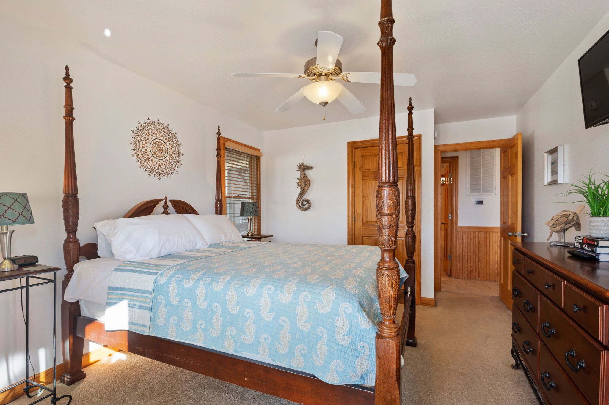 A four-poster bed with a ceiling fan, a wooden dresser, and a decorative wall piece.