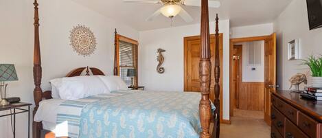 A four-poster bed with a ceiling fan, a wooden dresser, and a decorative wall piece.