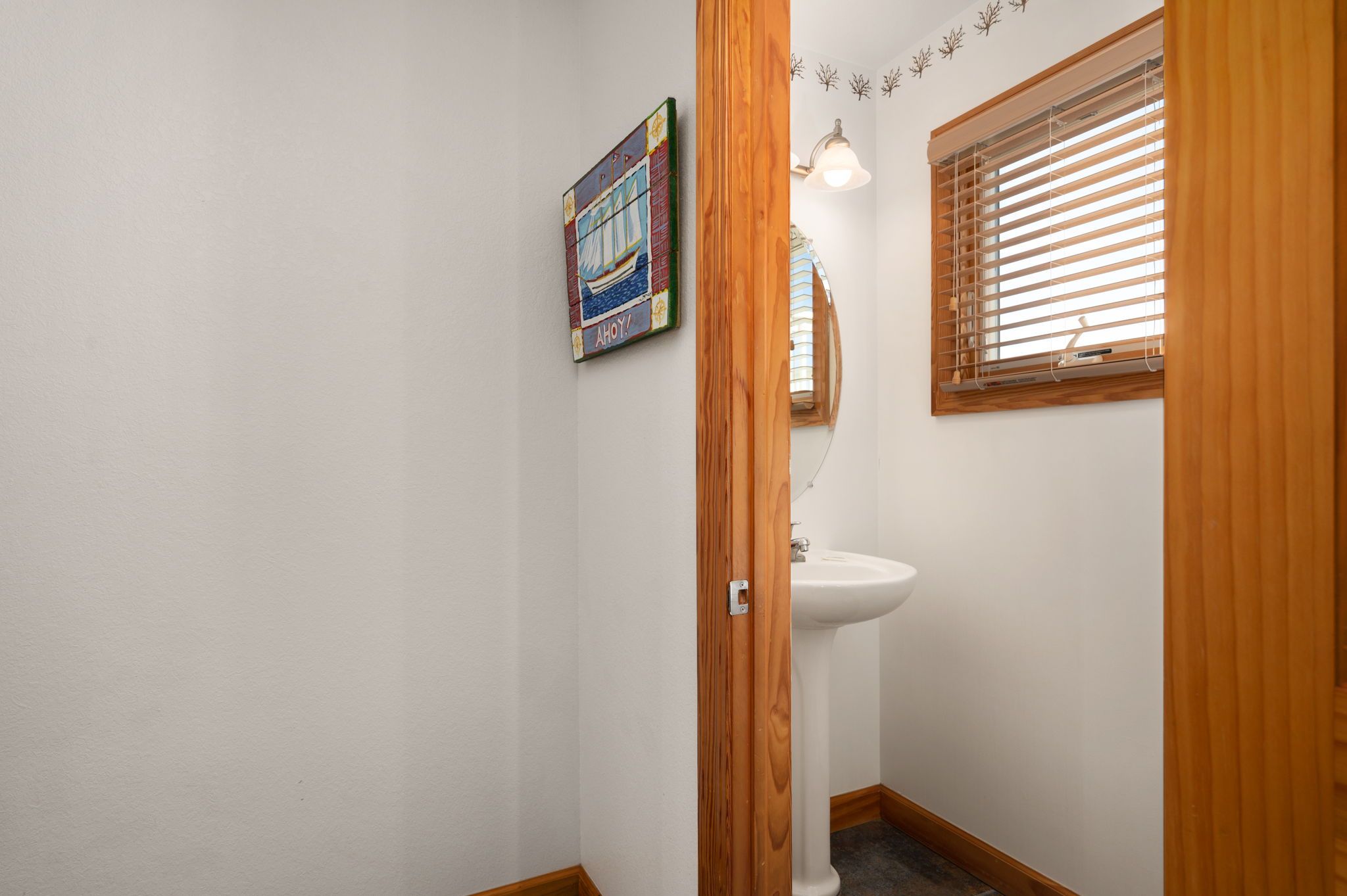 A bathroom with a white sink, wooden door frame, and a window with blinds.