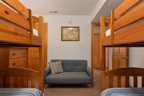 Una habitación con dos camas literas de madera, un sofá gris con un cojín a rayas y un mapa enmarcado en la pared.