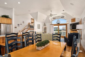 A dining area with a wooden table, chairs, and a plant centerpiece. A staircase with wooden railings leads to a lofted living area. - Seas The Day: Private Hot Tub, Amazing Sunsets (Nags Head)