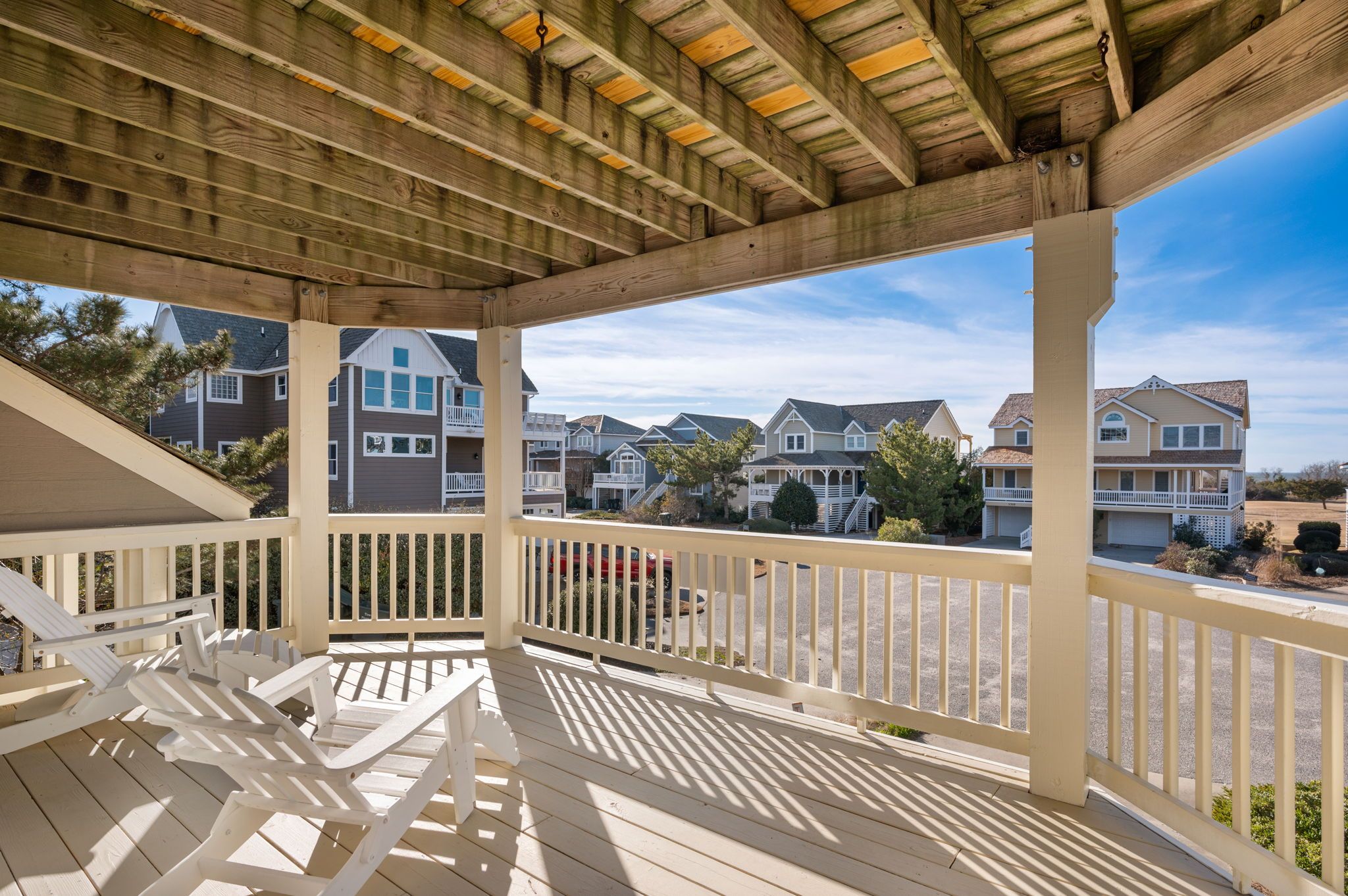 A covered deck with white railings and wooden beams, overlooking a row of townhouses.