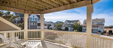A covered deck with white railings and wooden beams, overlooking a row of townhouses.