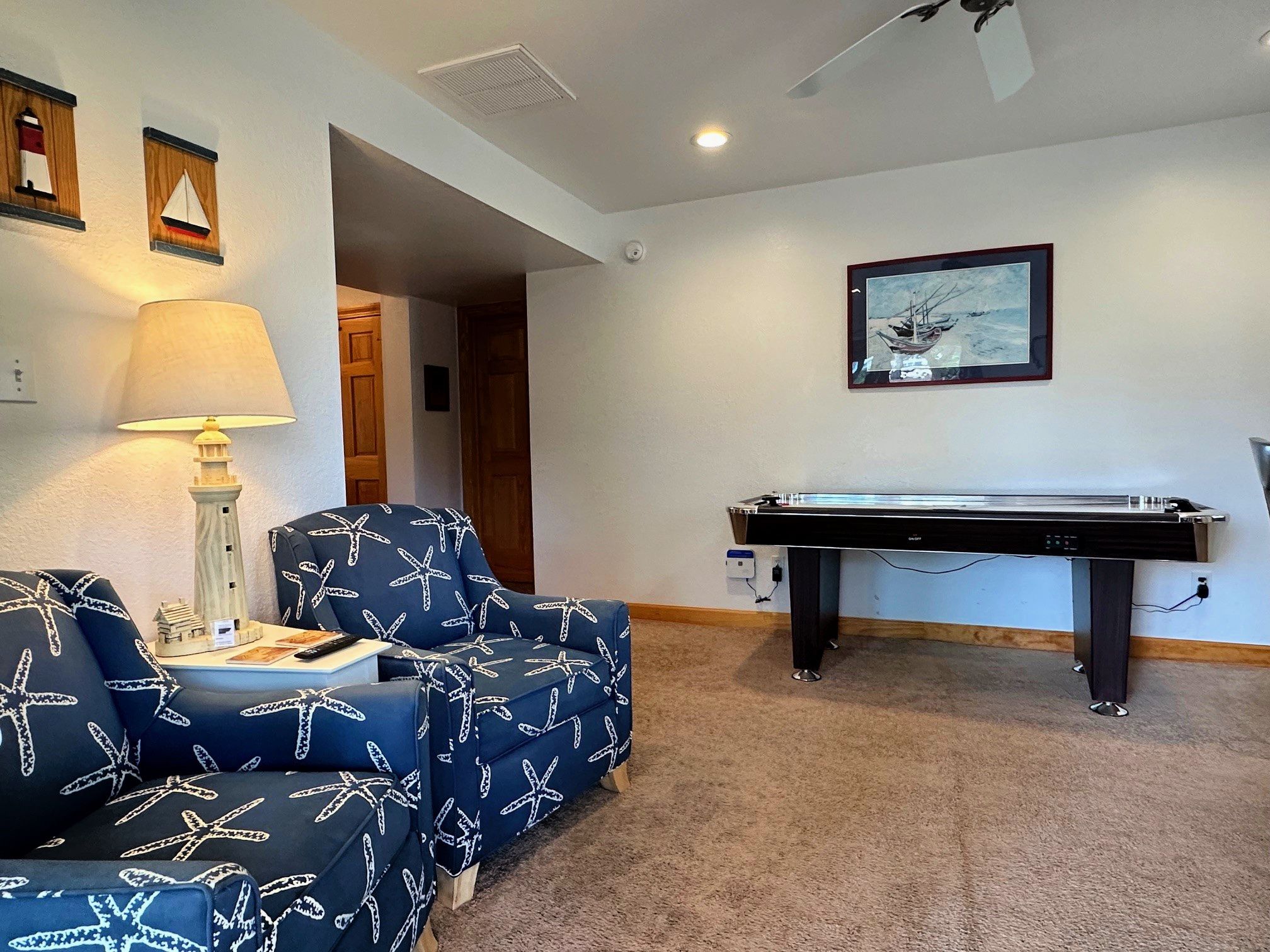 A room with a pool table, two blue armchairs with starfish patterns, a lamp, and a framed picture on the wall.