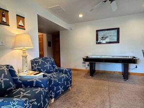 A room with a pool table, two blue armchairs with starfish patterns, a lamp, and a framed picture on the wall.