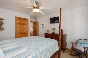 Un dormitorio con una cama con dosel, un aparador de madera, un televisor montado en la pared y un sillón mecededor.