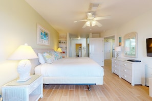 A bedroom with a bed, a nightstand, a dresser, a ceiling fan, and a door leading to another room.