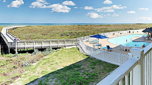 Un espace piscine avec vue sur l’océan, une terrasse en bois et une clôture blanche.