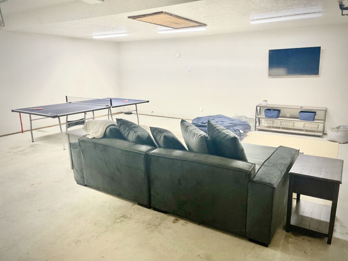 A room with a large grey sofa, a ping pong table, and a small wooden table.