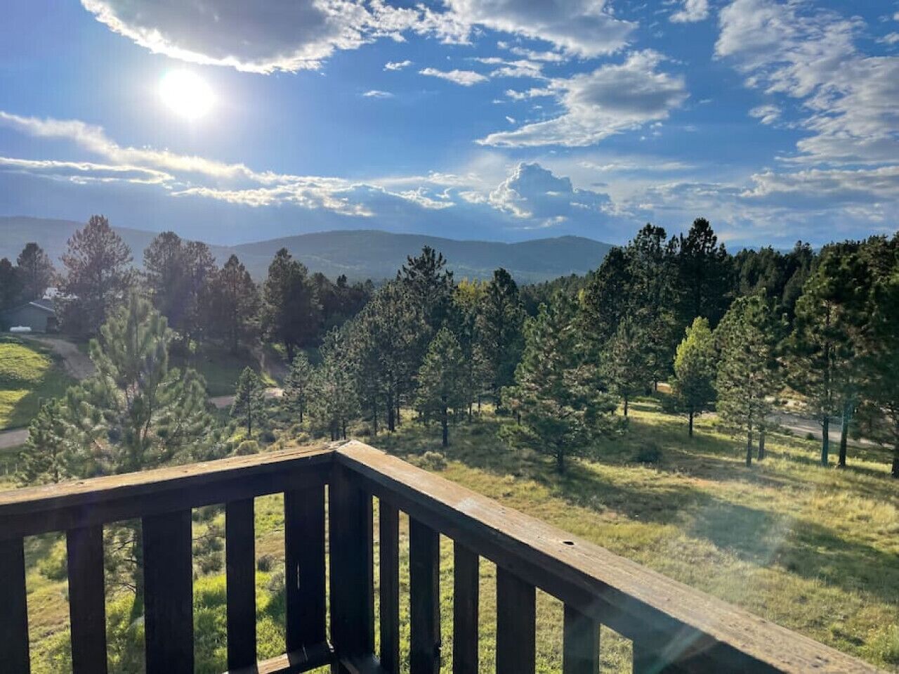 A wooden deck overlooking a grassy area with trees and distant hills.