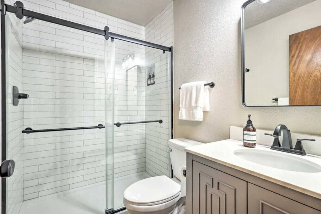 A modern bathroom with a glass shower enclosure, a white toilet, a sink with a mirror, and a towel hanging on the wall.