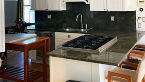 A modern kitchen with white cabinets, a central island with a stove, and a large range hood. - Amazing experience near the Quinnipiac River. Historic w/chef's kitchen & bidet. (New Haven)
